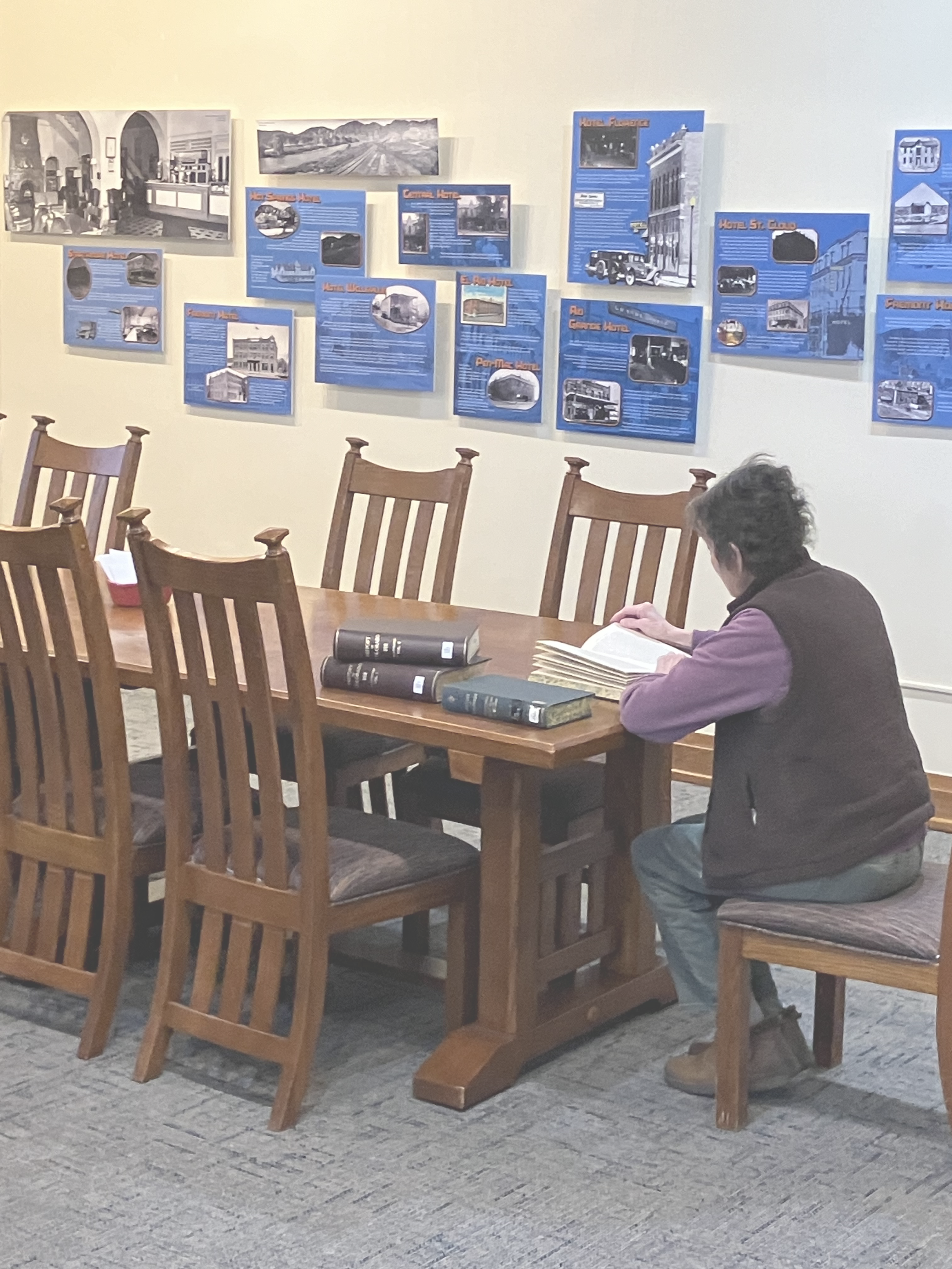 Color photo of museum Reading Room with woman reading books at a table.
