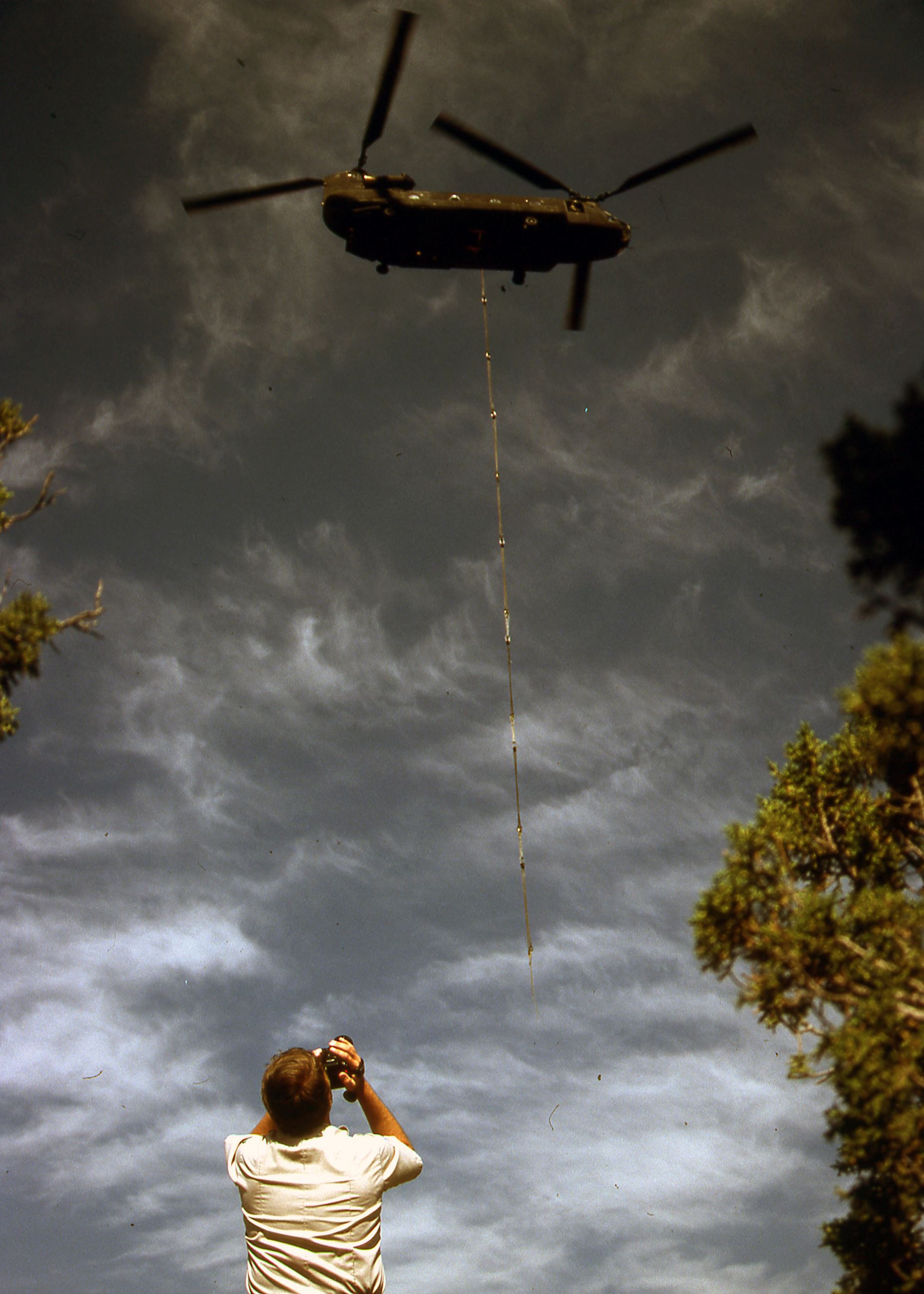 Color photo of a CH-47 Chinook helicopter hovering over a person on the ground. Circa 1992.